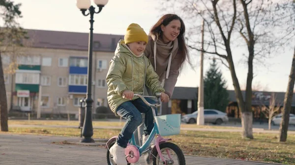 Мама вчить маленьку дитину їздити на велосипеді в місті, дитина їде на тротуарі, щаслива сім'я, дитина грає і сміється з мамою, вчиться їздити, змушує дитинство мріяти справжні дівчата, дочка і мама смішні — стокове фото