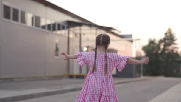 Una niña levantó las manos y mantiene el equilibrio, juegos infantiles en la calle, el niño se divierte, el niño camina por el bardyur en la ciudad, entretenimiento infantil activo en el patio — Vídeo de stock