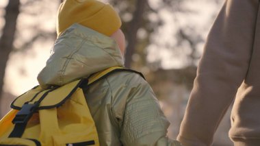 Anne sırtında bir sırt çantasıyla çocuğa liderlik eder, anne küçük çocuğu elinden tutar, çocuğu okula götürür, okul çantasıyla okul bahçesinde bir derse doğru yürür, mutlu bir aile.