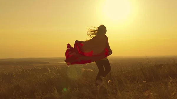 Happy teenage girl runs playing superhero at sunset, child on a green field in a red raincoat toy in the rays of light, childrens dream game, kid dreams of becoming a superhero in glare of the sun — Stock Photo, Image