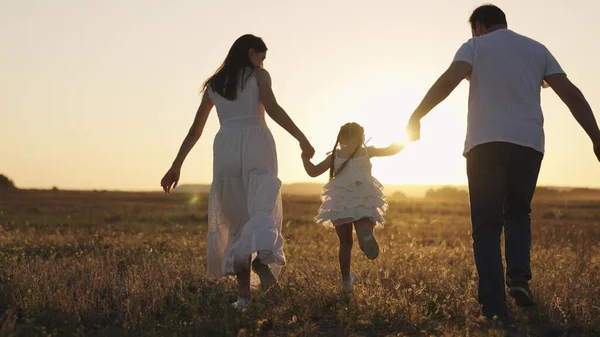 Little kid runs holding hand of mom and dad at sunset, cheerful child plays catch-up with his father and mother glare of sunlight, happy family, baby jumps high up glare of dawn travel nature outdoor — Stock Photo, Image