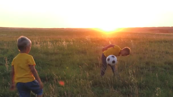 Meninos jogar futebol em um gramado verde ao pôr do sol, um campo de futebol, uma criança com uma bola ao sol, divirta-se com amigos em uma equipe, crianças felizes, sonho de infância de ser um jogador de futebol, filhos fantasia — Vídeo de Stock