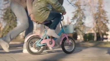 Küçük çocuk iki tekerlekli bisiklet sürmeyi öğreniyor, çocuk annesiyle şehir parkında oynuyor, mutlu aile, anne, bebekle sokaklarda eğleniyor, pedal çevirmeyi ve tekerlekleri çabucak öğreniyor, çocukluk hayalleri kuruyor.