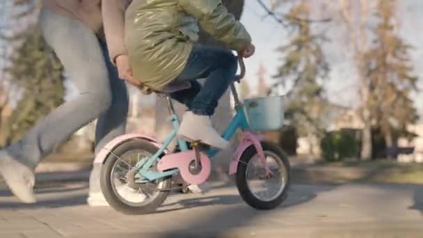 Criança aprende a andar de bicicleta de duas rodas, criança brinca com sua mãe no parque da cidade, família feliz, mãe, se divertir com o bebê na rua, girar pedais e rodas rapidamente, sonho de infância para aprender passeio — Vídeo de Stock