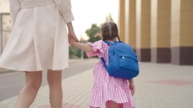 Sırt çantalı küçük bir çocuk annesini elinden tutup okula gidiyor. Annesi okul bahçesinde okul çantasıyla geziyor. Mutlu bir ailesi var.
