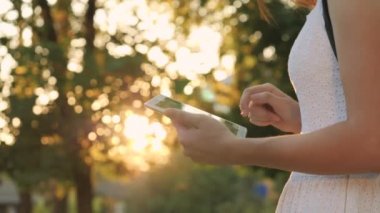 Genç bir kız elinde günbatımının parıltısıyla modern bir tablet tutuyor, internete giriyor, tabletin dokunduğu ekranda güneş ışınları parlıyor, modern teknoloji kavramı.
