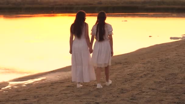 Happy women friends walk along beach at sunset, young mother and an adult daughter in rays of the sun, happy family, talking with cheerful person, friend of life, help with advice in kind atmosphere — Stock Video