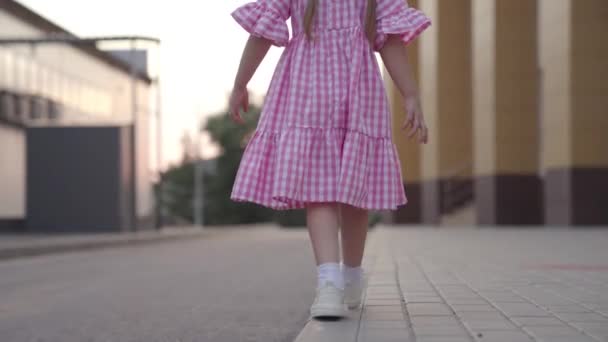 小さな女の子が手を上げてバランスを保ち路上で子供の遊び子供は楽しんで街の庭を歩く子供は庭で子供のエンターテイメント — ストック動画