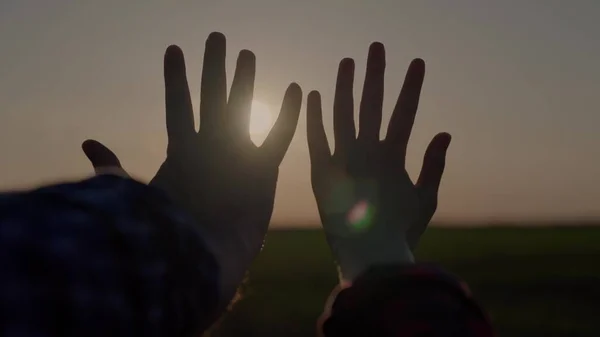 Hands at sunset, lovers reach for the sky, dream of a good, good desire of people, ask for help from the sun, pray in the rays of sunlight, bright glare through the fingers of peoples palms — Stock Photo, Image