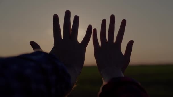 Hands at sunset, lovers reach for the sky, dream of a good, good desire of people, ask for help from the sun, pray in the rays of sunlight, bright glare through the fingers of peoples palms — Stock Video