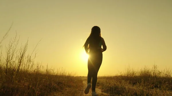 Happy girl runs to meet her dream at sunset, doing sports jogging at dawn, listening to music in an active morning jog in rays of sun light, taking care of her health and being in shape, human figure — Stock Photo, Image