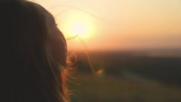 Girl prays looking at sunset, long hair is flying away in glare of sunlight rays in strong wind, looking at dawn, lonely hike of brave girl, looking into sky with her eyes, believing good — Stock Photo, Image