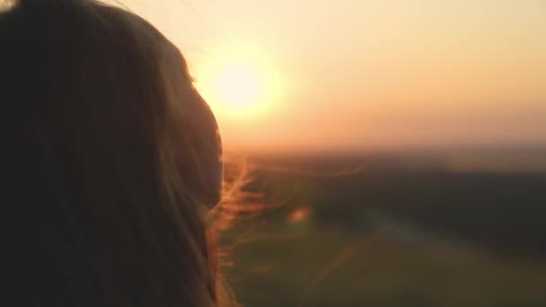 女の子は日没を見て祈る、長い髪は強い風の中で太陽の光のぎらぎらと飛んでいる、夜明けを見て、勇敢な女の子の孤独なハイキング、彼女の目で空を見て、信じて良い — ストック動画