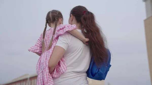 Matka nosí malou dceru s batohem v náručí do školy, učí dítě na základní škole, šťastnou rodinu, odvádí dítě se školní brašnou, získává znalosti o budoucím životě — Stock fotografie