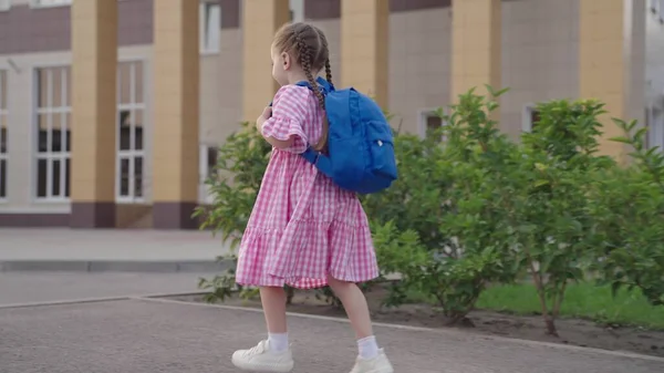 Pequena menina alegre corre escola com mochila em seus ombros, criança feliz está com pressa para a primeira lição, o bebê receberá educação pré-escolar primária, criança vai ganhar novos conhecimentos na sala de aula — Fotografia de Stock