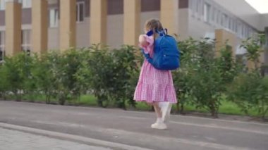 Küçük neşeli kız omuzlarında sırt çantasıyla okulu yönetiyor, mutlu çocuk ilk dersi almak için acele ediyor, bebek ilkokul eğitimi alacak, çocuk sınıfta yeni bilgiler kazanacak.