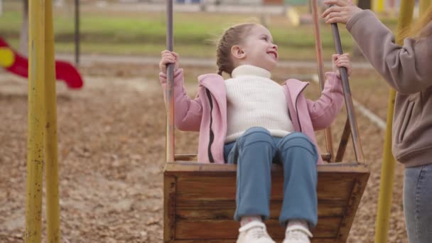 Küçük bir çocuk salıncakta sallanıyor ve uçarken gülüyor, bir sonbahar oyun parkı, mutlu bir aile, bir anne çocuğunu şehir parkında yuvarlıyor, çocukluk hayali uçuyor, annesine yürüyüş yaparken gülümsüyor, bir bebekle oynuyor. — Stok video