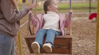 Anne küçük çocuğu sallıyor salıncakta, neşeli çocuk yukarı aşağı uçuyor, bebek oyun oynarken gülüyor ve gülümsüyor, anne kız parkta yürüyor, mutlu aile, çocukluk hayali uçuyor.