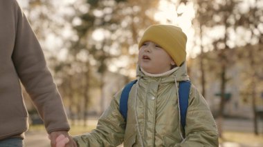 Sırt çantalı neşeli çocuk okula giderken annesini tutuyor, okul çantalı neşeli çocuk, birinci sınıf mutlu aile aceleyle ders veriyor, ana baba kenti sonbahar parkında bebek