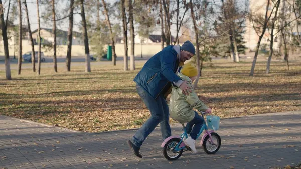 Радісний батько чайник маленька дитина їде на двоколісному велосипеді щаслива сім'я, дитинство мріє про їзду на велосипеді дитина тато грає весело міський парк, дитина крутить педалі колеса, батько займається верхи з дочкою — стокове фото