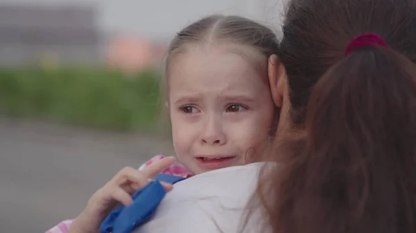Uma criança chora abraçando sua mãe, pequena criança chateada cai lágrimas no ombro de suas mães, uma mulher acalma sua filha manchada de lágrimas, lágrimas de seus olhos fluem para baixo rosto de meninas, sentimentos infantis de culpa — Fotografia de Stock