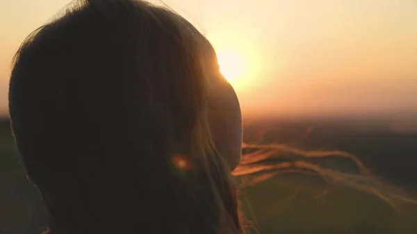 Girl prays looking at sunset, long hair is flying away in glare of sunlight rays in strong wind, looking at dawn, lonely hike of brave girl, looking into sky with her eyes, believing good — Stock Photo, Image