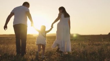Küçük kız anne ve babasının elini tutuyor ve gün batımında gökyüzünde koşuyor, mutlu aile hayatı gün ışığında, anne babasıyla çocuk gezide eğleniyor, neşeli çocuk çabuk anne ve babayla hasret gideriyor.