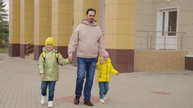 Baba, sırt çantalı çocukları okul bahçesinden geçirir, birinci sınıf öğrencilerini eğitir, küçük çocukları acele ettirir, anaokulu eğitimine başlar, kızlarını anaokulundan alırlar.