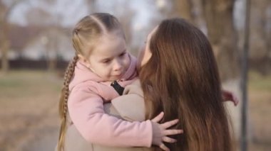 Küçük çocuk annesinin kollarında otururken boynuna sarılıyor, mutlu aile, yorgun çocuk annesine tırmanıyor, anne babasıyla kucaklaşıyor, üzgün kız dışarıda dinleniyor, şehir parkında.