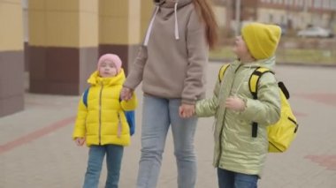 Anne, sırt çantalı çocukları okula götürüyor, mutlu aile, okul çantalı çocuk hemen derse koşuyor, okul zili çalıyor, bebekler ilkokula gidiyor, çocuklar eğitim görüyor.