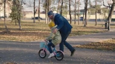 Baba çocuk bisikleti, kız pedalları ve tekerlekleri öğretiyor. İki tekerlekli araç, eğlence parkı, mutlu aile, baba ve çocuk. Boş günlerinde birlikte rahatlıyorlar.