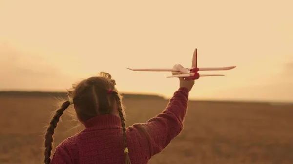 Mutlu çocuk gün batımını oyuncak uçakla, çocukluk rüyası uçuyor, çocuk havada süzülüyor paletleri hayal ediyor, hava taşımacılığı pilotu oluyor, kanatları havada uçuyor, kız kanatları açık güneşi sunuyor.