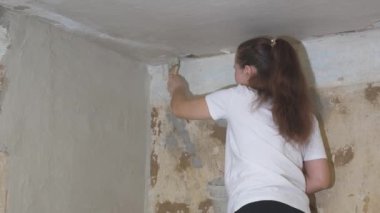 Kadın sıvacı duvarı fırçayla kaplıyor, bir apartmanın yenilenmesi, endüstriyel inşaat müteahhiti, çimento işi teknolojisi, kirli aletlerle bitiriyor, beton kaldırımla inşa ediyor.