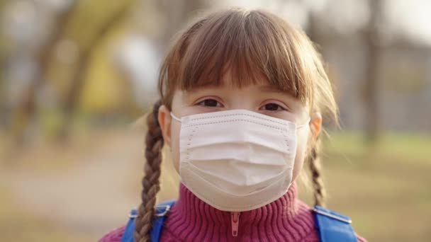Κορίτσι ιατρική μάσκα με χαμόγελα σακίδιο, μικρό παιδί σχολείο προστατεύεται από covid 19, κρατήσει υγιή αναπνοή παιδί απωθεί τα μικρόβια, μωρό σχολείο τρόπο ζωής, πανδημία νηπιαγωγείο, φορώντας προστατευτικό πρόσωπο — Αρχείο Βίντεο