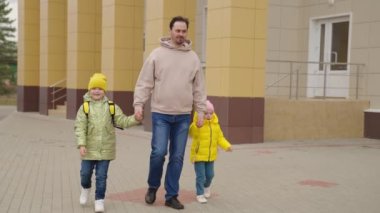 Baba, sırt çantalı çocukları okula, okul bahçesine, baba ve kızları sınıfa birlikte koşuyor. Mutlu aile, okuldan sonra çocuğu okula götürüyor, anaokulu eğitimi...