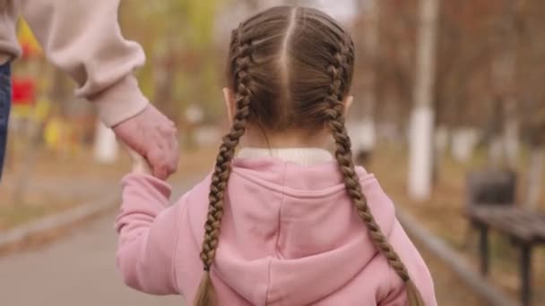 Padre lleva a la niña a mano a través del parque de la ciudad de otoño, niño feliz familia, día del padre, niño pequeño con coletas en la cabeza se aferra a la palma de los papás, hombre con hija sobre fondo naranja dorado — Vídeos de Stock