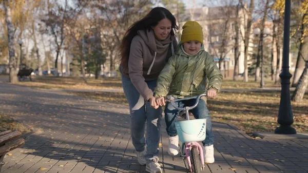 Mãe ensina criança a andar de bicicleta na cidade, passeios de criança na calçada, família feliz, brincadeiras de bebê e ri com a mãe, aprender passeio, tornar o sonho da infância realidade meninas, filha e mãe são engraçados — Fotografia de Stock