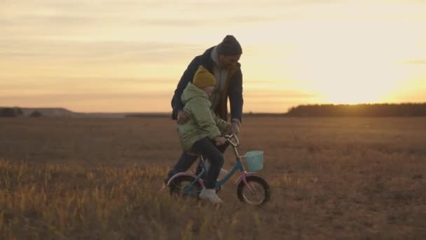 Ребенок с папой учится ездить на велосипеде на закате, счастливая семья, ребенок и папа спин-педали и колеса в свете солнца, ребенок учится ездить на природе, весело детство, играть на выходные с родителями на открытом воздухе — стоковое видео