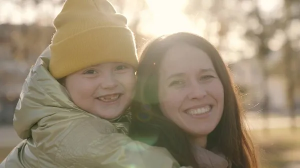 Mother and child hug at sunset of autumn in city, happy family, mother and kid laugh in their arms in light of sun, cheerful parent with baby daughter in bright highlights, childhood life little girl — Stock Photo, Image