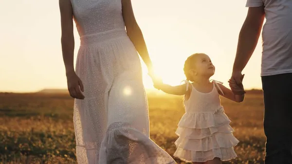 Happy baby smiling at sunset with parents, mother, father and child walk in the sun, hold kid by hands, young family, taking care of their little daughter, family walk in evening park in orange light — Stock Photo, Image