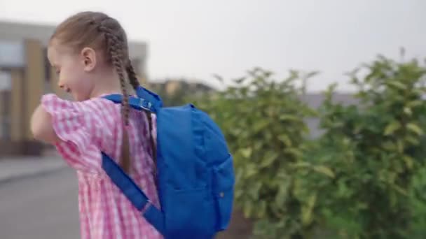 Маленькая веселая девочка бежит в школу с рюкзаком на плечах, счастливый ребенок спешит на первый урок, ребенок получит начальное дошкольное образование, ребенок получит новые знания в классе — стоковое видео