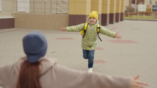 Sırt çantalı küçük bir kız çocuğu koşuyor annesine sarılıyor, çocuk derslere seviniyor, mutlu bir aile, okul çantası arkasında gülen bir çocuk annesine koşuyor, okul bahçesinde koşuyor. — Stok video