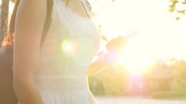 Genç bir kız elinde günbatımının parıltısıyla modern bir tablet tutuyor, internete giriyor, tabletin dokunduğu ekranda güneş ışınları parlıyor, modern teknoloji kavramı.