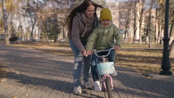 Mama uczy małe dziecko jeździć na rowerze w mieście, dziecko jeździ na chodniku, szczęśliwa rodzina, dziecko bawi się i śmieje się z mamą, uczyć jazdy, sprawiają, że marzenia z dzieciństwa się spełniają dziewczyny, córka i mama są zabawne — Wideo stockowe