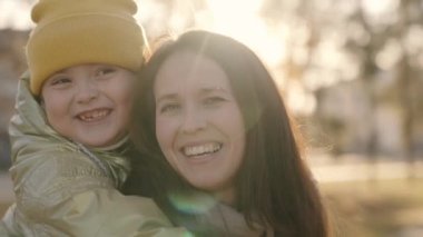 Anne ve çocuk, sonbaharın günbatımında birbirlerine sarılırlar. Mutlu aile, anne ve çocuk, güneş ışığında kollarında gülerler. Neşeli bir ebeveyn ve parlak röfleler içinde küçük bir kız çocuğu.
