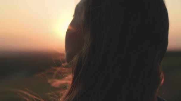Dziewczyna modli się patrząc na zachód słońca, długie włosy odlatują w blasku promieni słonecznych w silnym wietrze, patrząc na świt, samotna wędrówka odważnej dziewczyny, patrząc w niebo oczami, wierząc w dobro — Wideo stockowe