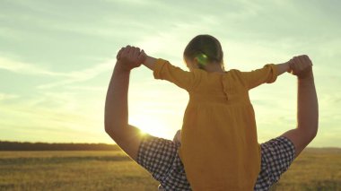 Neşeli küçük çocuk gün batımında babasına biniyor, neşeli çocuk babasının omuzlarına oturuyor güneş ışığında, mutlu aile, haftasonu gezisinde ebeveynli kız, çocukluk hayali pilot olmak ve uçmak.
