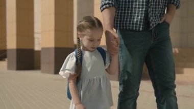 Baba küçük bir kızı okula götürüyor, sırt çantalı bir kız babasının elini tutuyor, bir çocuk okulu eğitim sistemi, mutlu bir aile, mutlu bir ebeveyni olan neşeli bir çocuk