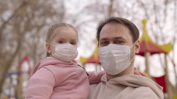 Père tenant un enfant dans un masque de protection médicale ses bras, famille heureuse, embrasser papa, protéger petit enfant contre la pandémie de coronavirus, vie covid-19, bras de bébé d'un parent sur aire de jeux gros plan — Video