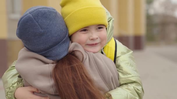 Mor möter barn med ryggsäck från skolan, barn med skolväska kramar en mamma på skolgården, barn kärlek till förälder, första klass efter grundskolan, student av utbildningscentrum — Stockvideo